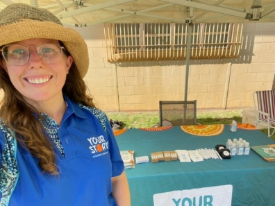 Smiling woman wearing hat in front of table laid with Your Story promotional material