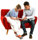 two people sitting on a red couch looking at a submission